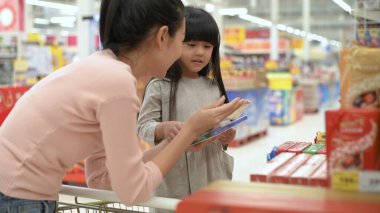 Alışveriş konsepti. Asyalı anne ve kızı alışveriş merkezinde çikolata satın alıyor. 4k Çözünürlüğü.