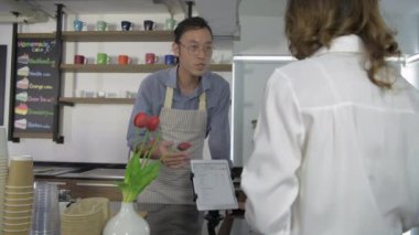 Barista konsepti. Erkek garson müşteriye tabletle menüyü sunuyor. 4k Çözünürlüğü.