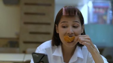 Asyalı bir kadın evin içinde kızarmış tavuk yiyor. 4k Çözünürlüğü.