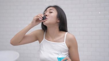 Günlük rutin konsept. Genç Asyalı kadın banyoda gargara yapıyor. 4k Çözünürlüğü.