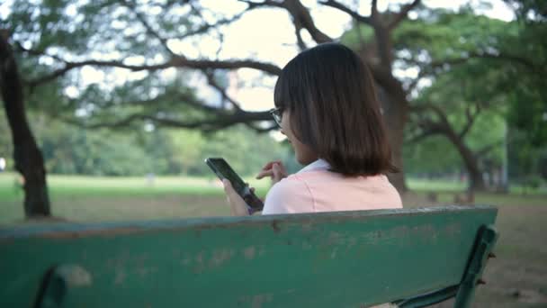 Σχέδιο Διακοπών Μια Ασιάτισσα Κάθεται Ένα Κινητό Τηλέφωνο Στον Κήπο — Αρχείο Βίντεο