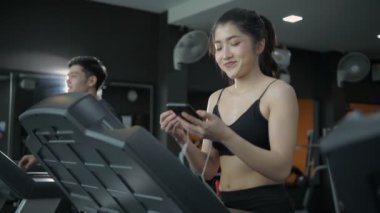 Fitness konsepti. Koşu bandında koşan ve spor salonunda müzik dinleyen genç Asyalı kadın. 4k Çözünürlüğü.
