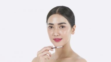 Güzellik konsepti. Asyalı bir kız beyaz bir arka planda dudaklarını rujla boyuyor. 4k Çözünürlüğü.