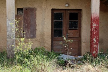 Sıcak güneşli bir gün önünde büyümüş çim ve diğer bitkiler ile kırık harap cephe ile duvara kaplanmış pencere ile terk edilmiş ev ön girişi