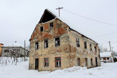 Kırık pencereler, düşmüş cephe ve duvarlar tuğla, soğuk kış gününde asfalt yolun yanında derin kar kaplı terkedilmiş eski harap ev