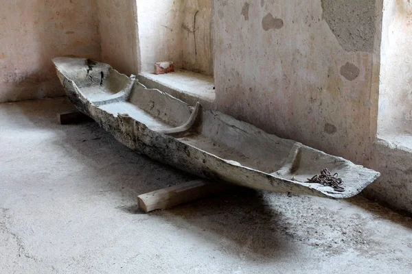 Ancient petrified wooden river boat with chain in front set aside on wooden logs in old castle room with dilapidated walls waiting for exhibition