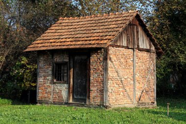 Arka bahçesinde eski kırmızı tuğla depolama yapısı ile harap ahşap kapılar ve pencere yeşil çim ve yoğun ağaçlar ile çevrelenmiş