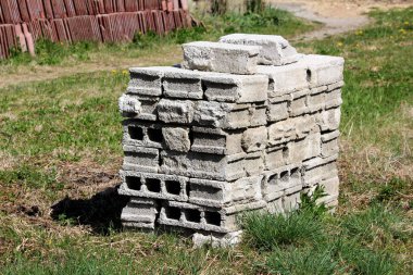 Sıcak güneşli bahar gününde arka planda çatı karoları ve küçük çiçekler ile kesilmemiş çim çevrili arka bahçede koymak kullanılmış gri inşaat yapı taşları yığını