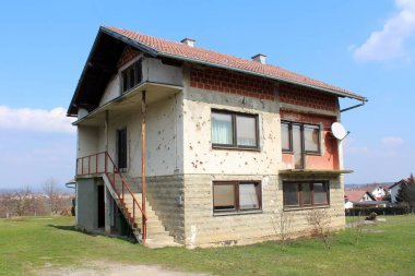 Kış çim ve kurutulmuş ağaçlar ile çevrili düşen cephe, görünür yapı taşları, yeni pencereler, kapılar ve drenaj boruları ile savaş sırasında şarapnel tarafından hasar aile evi