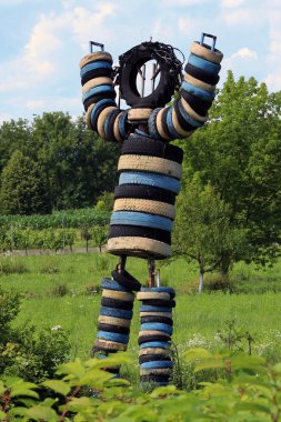 Çeşitli renklerde eski lastiklerden yapılmış büyük heykel sıcak güneşli bir günde büyük çim alanında koymak havada eller ile kişi ayakta gibi bakmak için yapılan