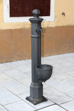 Sıcak güneşli bir gün eski aile evinin yanında yerel kasaba meydanının taş fayans üzerine monte el su pompası olarak hizmet barok tarzı demir boru