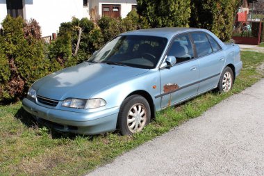 Eksik plaka ile kırık ve paslı parçalar ile araba evin önünde sol ve hedge almak için bekleyen ve geri dönüşüm için yerel araba hurdalığa sürücü