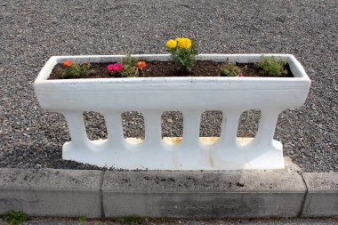 Koyu gri çakıl ile çevrili frenlemek yanında çeşitli renkler küçük çiçekler ile beton beyaz çiçek kutusu