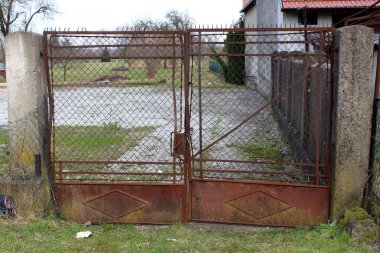 Paslanmış ve kısmen bükülmüş metal ve tel kapılar zincir ve ön kesilmemiş çim ile küçük asma kilit ile kilitli