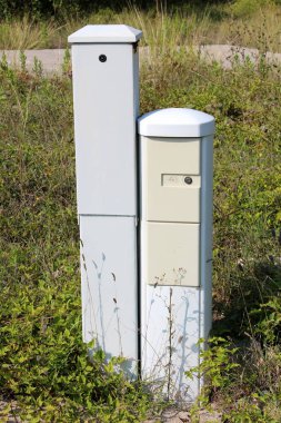 İki dar uzun boylu açık gri kilitli elektrik kutuları uzun boylu kesilmemiş çim ve sıcak güneşli günde terkedilmiş sanayi kompleksi diğer bitki örtüsü ile çevrili