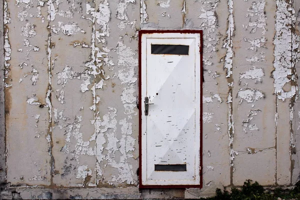 Partially rusted metal white door with two small openings on dilapidated fallen facade wall