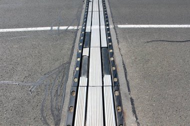 Sıcak güneşli bir günde kırık asfalt ve beyaz çizgi ile çevrili son derece kullanılan yıpranmış metal ve kauçuk köprü segmentleri bağlantısı