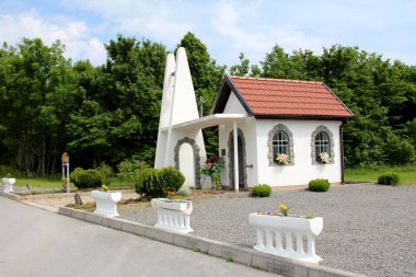 Yeni inşa edilmiş beton ve taş beyaz Şapel çiçek kutuları, küçük bitki örtüsü, ağaçlar ve çakıl otopark çiçekler ile çevrili