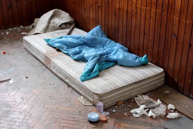 Eski yatak, kapak, sopa, el losyonu, açık prezervatif sarmalayıcıları, dokular, eski gazete, kırık cam ve evsiz ve bağımlıları tarafından kullanılan çöp ile terk edilmiş Oda