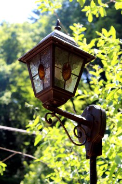 Antika koyu sokak lambası yapılmış temperli demir ve boyalı cam önünde yeşil yaprakları arka plan