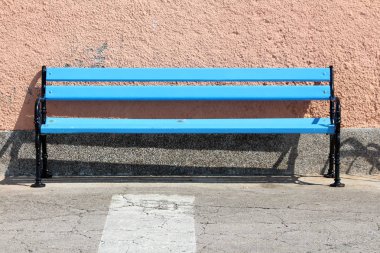 Siyah demir çerçeve ile uzun mavi ahşap kamu tezgah sıcak güneşli gün ev duvarının önünde Asfaltlı kaldırım tarafında monte