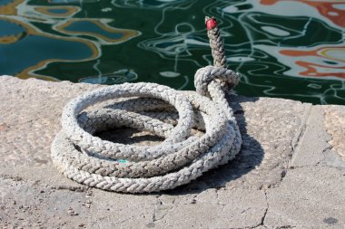 Sıcak güneşli gün yağlı yansıma ile sakin deniz yanında taş iskele kenarında sol güçlü beyaz ağır kullanılan halat