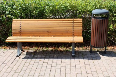 Sıcak güneşli gün yoğun hedge önünde benzer tarz kamu çöp yanında metal destekler ile taş fayans üzerine monte yoğun dar ahşap tahtalar yapılmış kamu tezgah