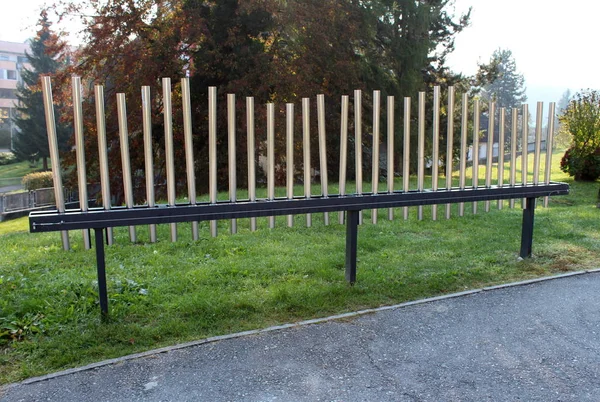 Public installation of musical pipes in various sizes that can be played to simple melody surrounded with paved path and uncut grass on warm sunny day