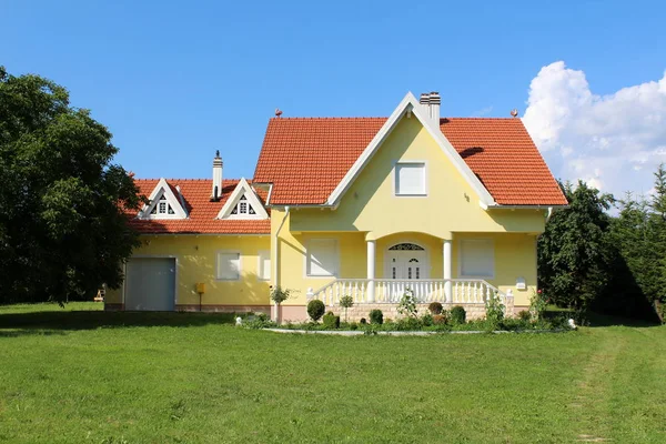 Ön ve küçük garaj yanında taş merdiven ile modern küçük sarı banliyö aile evi sıcak yaz gününde yeşil çim ve büyük ağaçlar ile çevrili