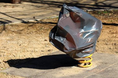 Yerel oyun alanında beton fayans ile çevrili soğuk kış aylarında koruma için siyah naylon ile kaplı beyaz kolları ile kırmızı midilli bahar binici salıncak şeklinde açık kamu oyun ekipmanları