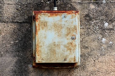 Kısmen paslanmış harap kilitli metal elektrik kutusu sıcak bahar gününde kalın siyah elektrik tel ile bağlı kırık yaşlı beton duvara monte