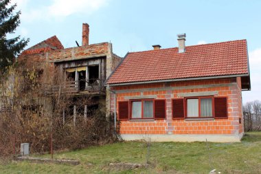 Tamamen büyümüş ön bahçe ile eski tamamen hasarlı harap evin yanında inşa tamamlanmamış yeni banliyö aile evi