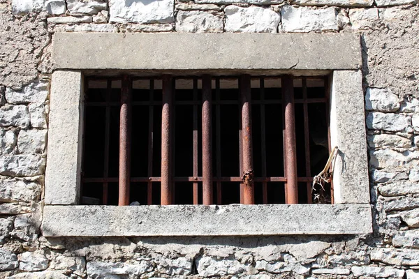 Stone window with massive frame and hard rusted metal bars in traditional stone wall