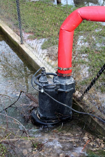 Su Pompası tel çit üzerinde büyük kırmızı hortum aracılığıyla sel sırasında bahçeden su pompalama