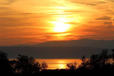 Sıcak güneşli bulutlu gün sakin deniz ve yoğun ağaçlar ile çevrili küçük bir adada dağ üzerinde bulutlu gökyüzünde günbatımı
