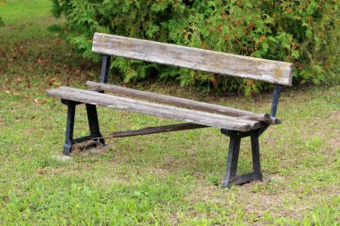 Harap ahşap tahtalar ve sıcak güneşli gün arka planda taze kesilmiş çim ve yoğun Bush ile çevrili güçlü metal destekler ile kırık eski kamu tezgah