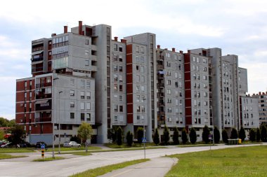 Her katta birden fazla daire ve onun önünde çim alanı ve yol sağ ile farklı boyutlarda birçok pencere ile eski endüstriyel görünümlü beton daire bina