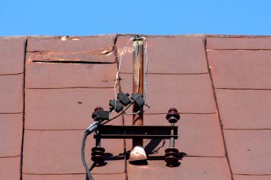 Kırık seramik izolatörler ile paslanmış metal kutup ve açık mavi gökyüzü arka planda paslanmış metal çatı fayans asılı elektrik Powerline telleri kesti