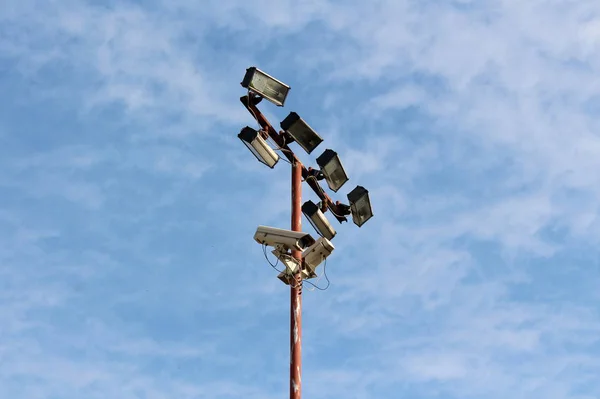 曇りの青空の背景に電線で接続された複数の光反射器とセキュリティカメラを備えた高金属ポール — ストック写真