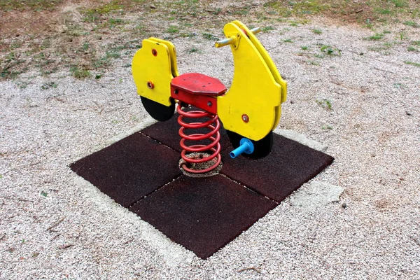 Outdoor public playground equipment in shape of wooden vintage looking motorcycle spring rider surrounded with protective rubber and playground sand