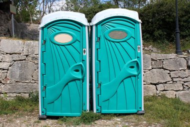 Geleneksel taş duvar ve çim alanının önünde erkek ve kadınlar için ayrılmış modern tasarım taşınabilir tuvaletler