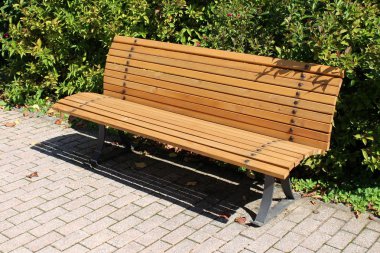 Sıcak güneşli bir gün arka planda yoğun yaprakları ile çevrili metal desteği ile taş fayans üzerine monte yoğun dar ahşap panoları yapılmış yeni kamu tezgah