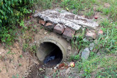 Toprak, kırmızı tuğla ve kırık beton ile kaplı beton kanalizasyon boru çıkış sıcak yaz gününde kesilmemiş çim ve küçük Bush bitki ile çevrili küçük köprü olarak kullanılan