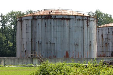 Küçük beton duvar, kesilmemiş çim, ağaçlar ve diğer orman bitki örtüsü üzerinde paslı metal köprü ile çevrili büyük metal paslanmış depolama Silo