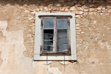 Kırık cam ile terk edilmiş evde ahşap pencere cephe ve sıcak güneşli günde ev duvarının görünür yapı taşları ile çevrili paslı metal menteşeler ile kırık çerçeve üzerine monte