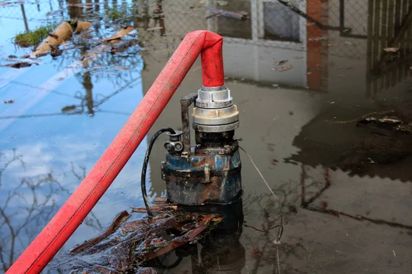 Arka planda ev ve gökyüzü yansıması ile büyük kırmızı hortum yoluyla sular altında bahçede su pompalama kısmen daldırma Su Pompası