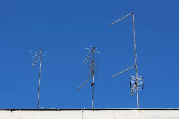 澄んだ青空の背景にアパートの上に金属の棒に取り付けられたさまざまな形状や形状の様々な複数のテレビアンテナ — ストック写真