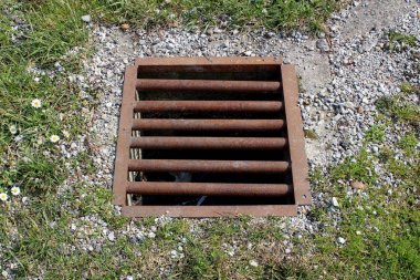 Kesilmemiş çim, küçük çiçekler ve çakıl ile çevrili yerel kanalizasyon bağlı güçlü paslanmış metal çubuklar ile fırtına drenaj