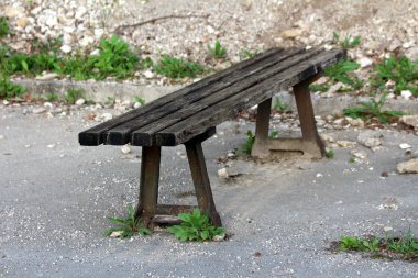 Sıcak güneşli bahar gününde kayalar ve kesilmemiş küçük bitkiler ile çevrili terk edilmiş park yeri asfalt kenarına monte güçlü paslı metal destekler ile eski ahşap kamu tezgah