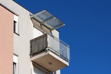 Modern apartman köşe balkon gri metal güvenlik çit ve kapalı pencere panjur şeffaf cam gölgelik ile sıcak güneşli bahar gününde kaplı çevrili